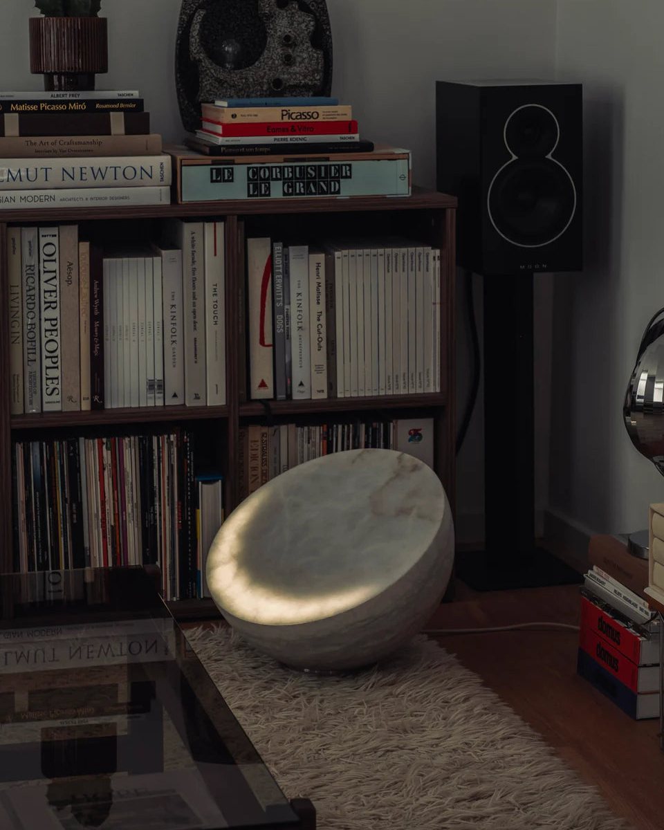 MOON Forty leuchtet auf einem Teppich neben Bücherregalen und einem Lautsprecher.