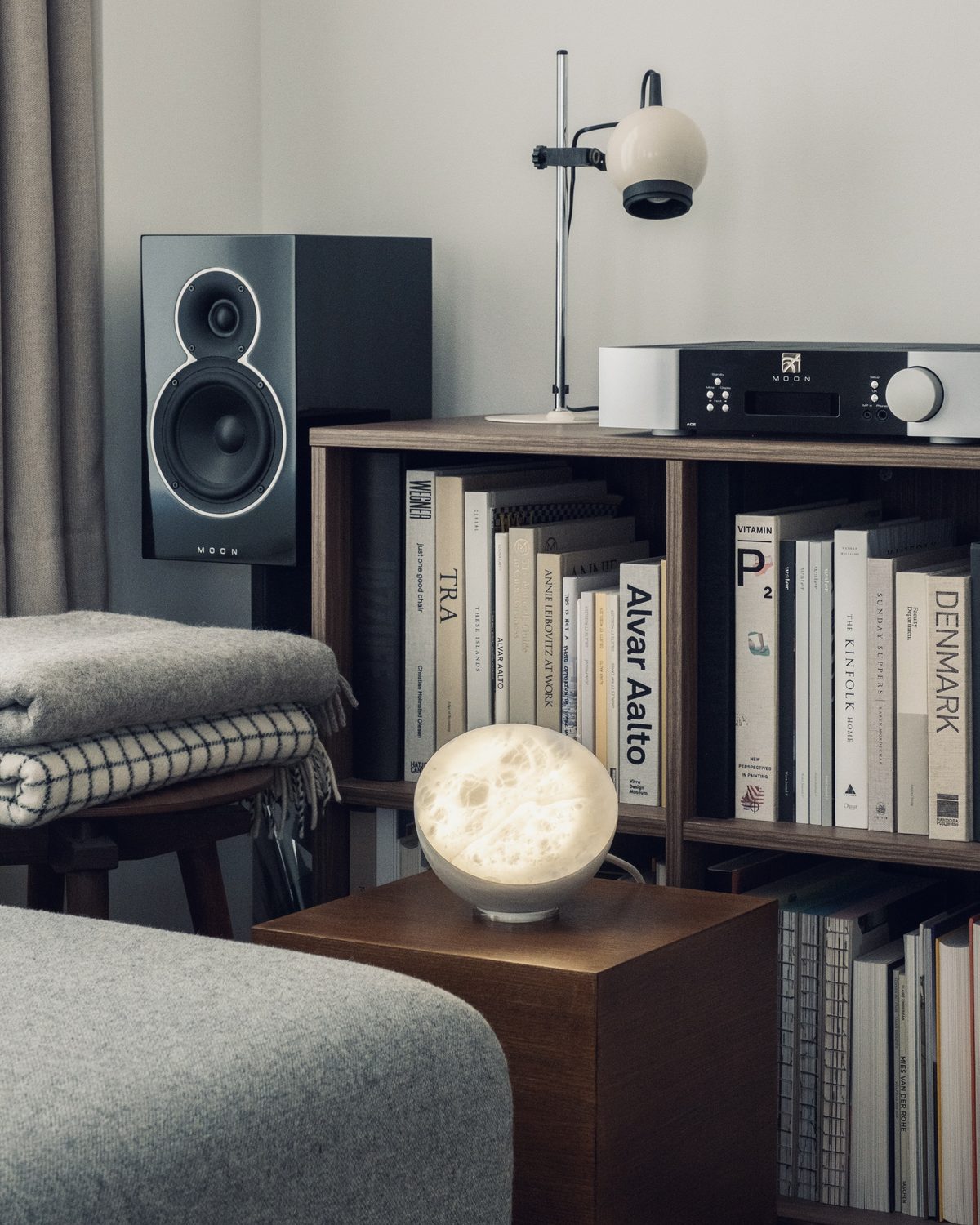 MOON Sixteen Alabaster lit on a side table by a bookshelf and speakers